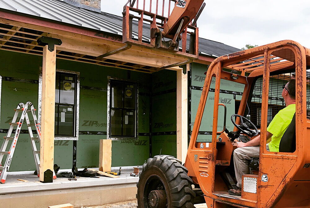 man in yellow shirt using orange forklift outside to hold up beam on house