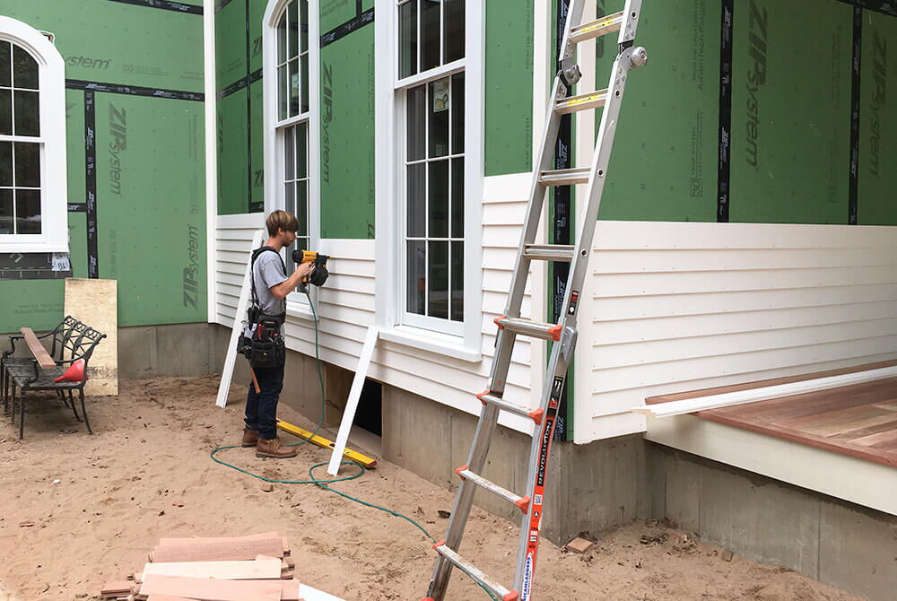 man installing white siding outside and using nail gun