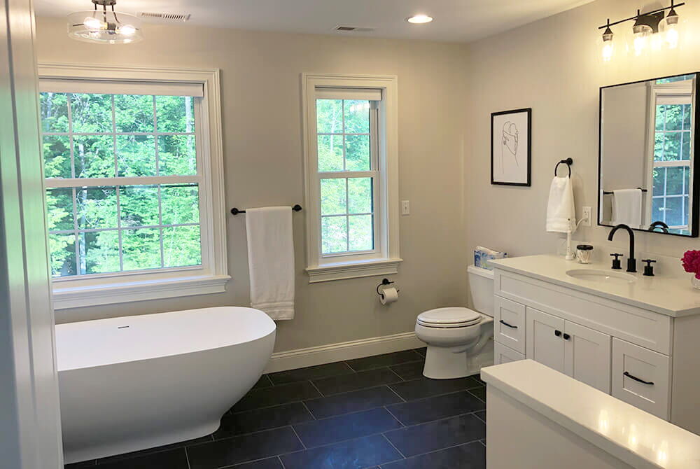 bathroom with black floor tiles and white soaker tub and white single vanity