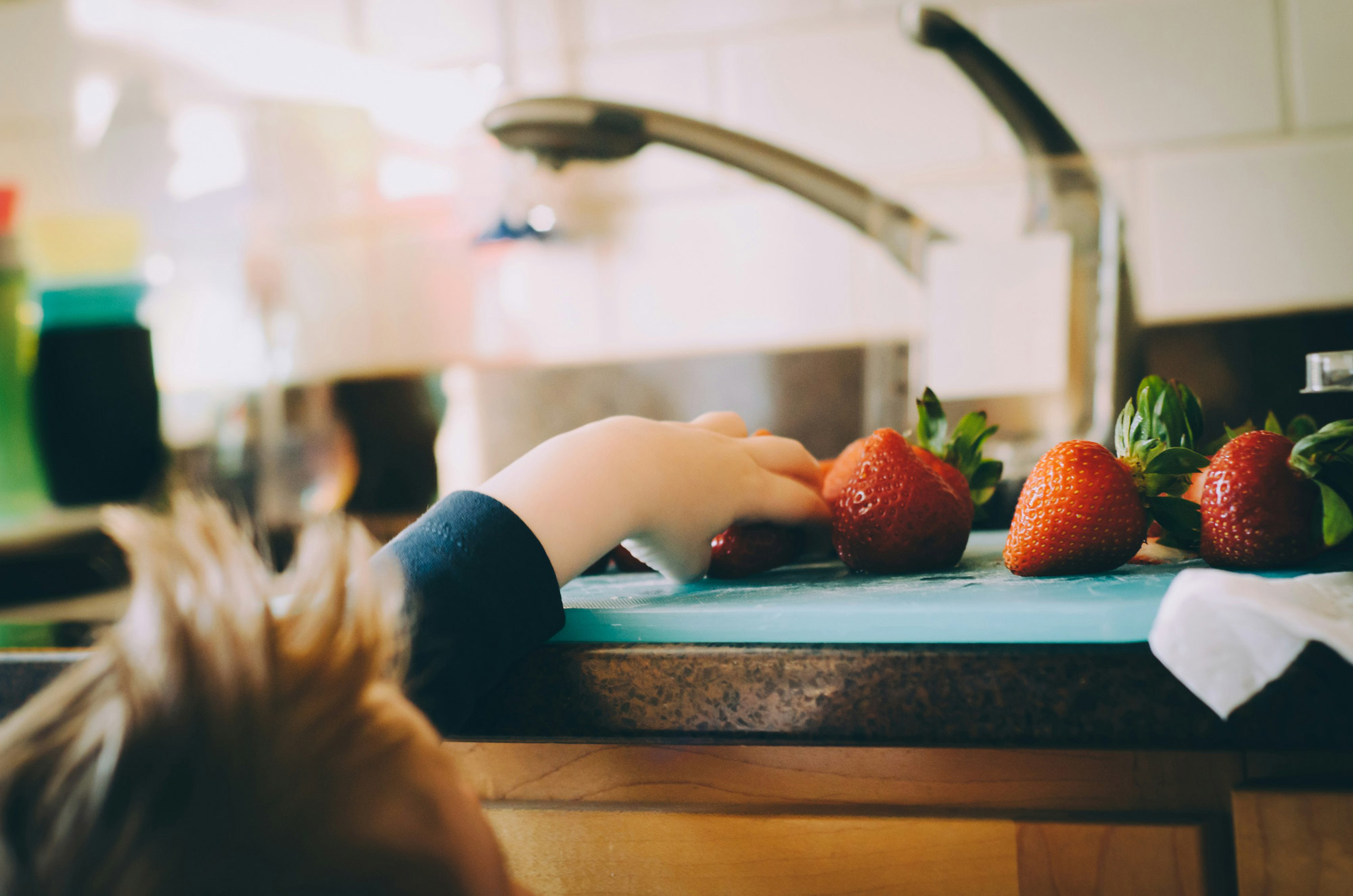 Boy getting strawberry on a kitchen counter